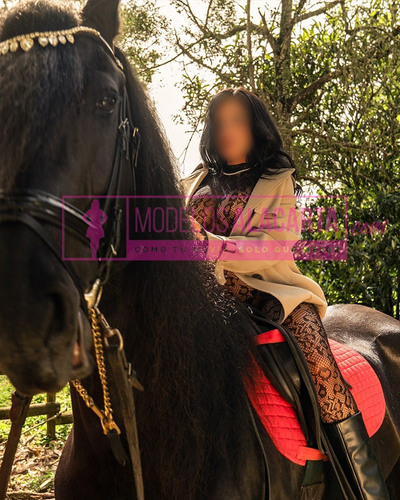una de las acomáñantes en Medellín, Naty Gold, posando con un caballo de manera poderosa y elegante, destacando su confianza y presencia imponente.